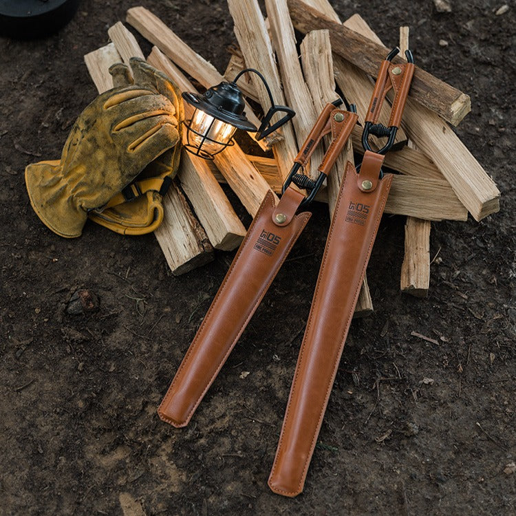 camping fire tongs with leather storage case portable outdoor tool sheaths on a wooden pile with a lantern and gloves in the background.