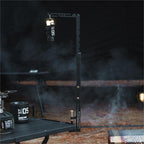 Outdoor camping lantern stand providing lighting beside campfire and cooking setup.