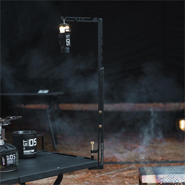 Outdoor camping lantern stand providing lighting beside campfire and cooking setup.