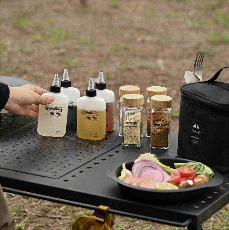 Outdoor cooking setup with seasoning bottles and a salad on a portable grill